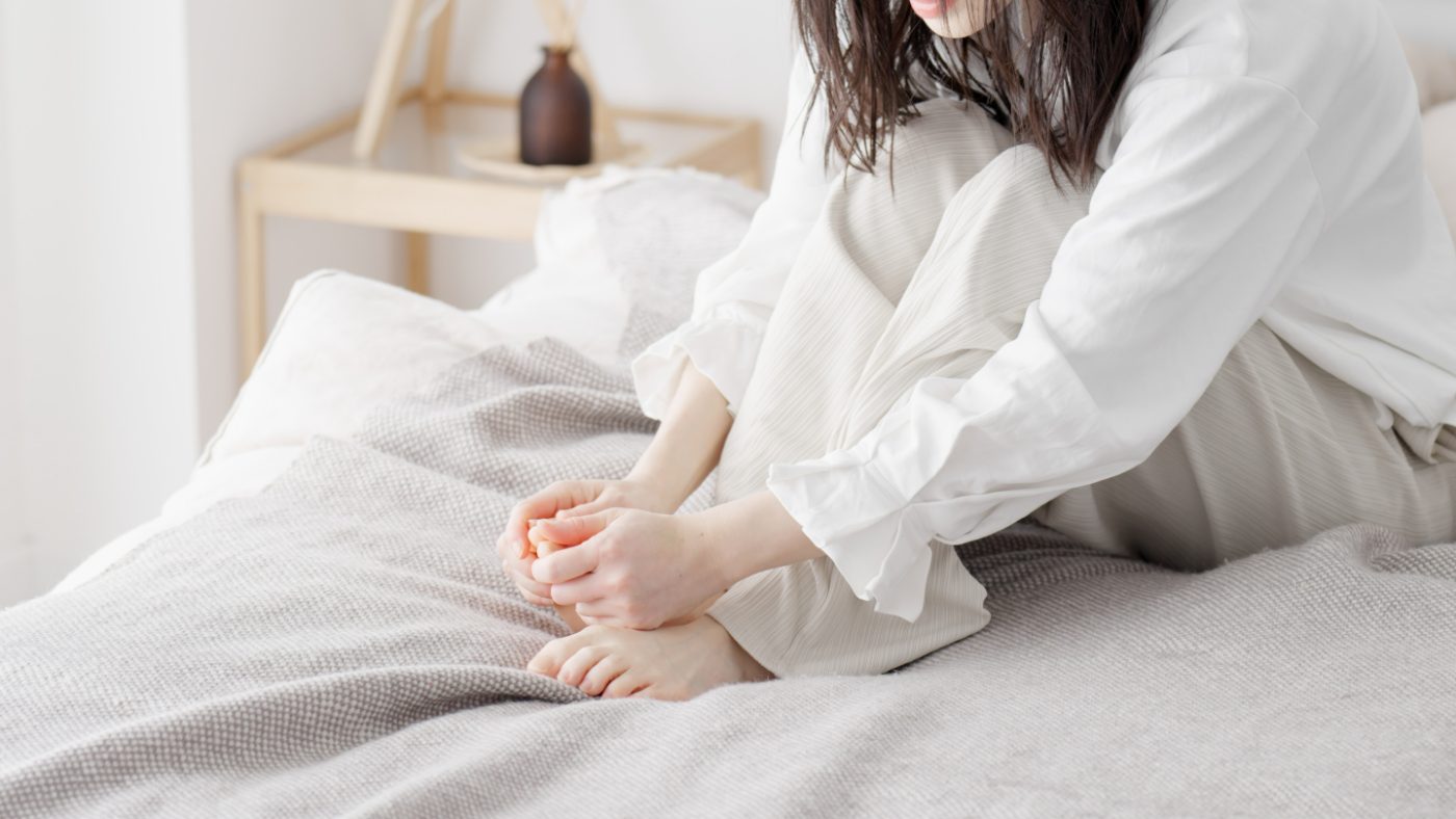 朝、ベッドの上で足先の冷えをほぐす女性